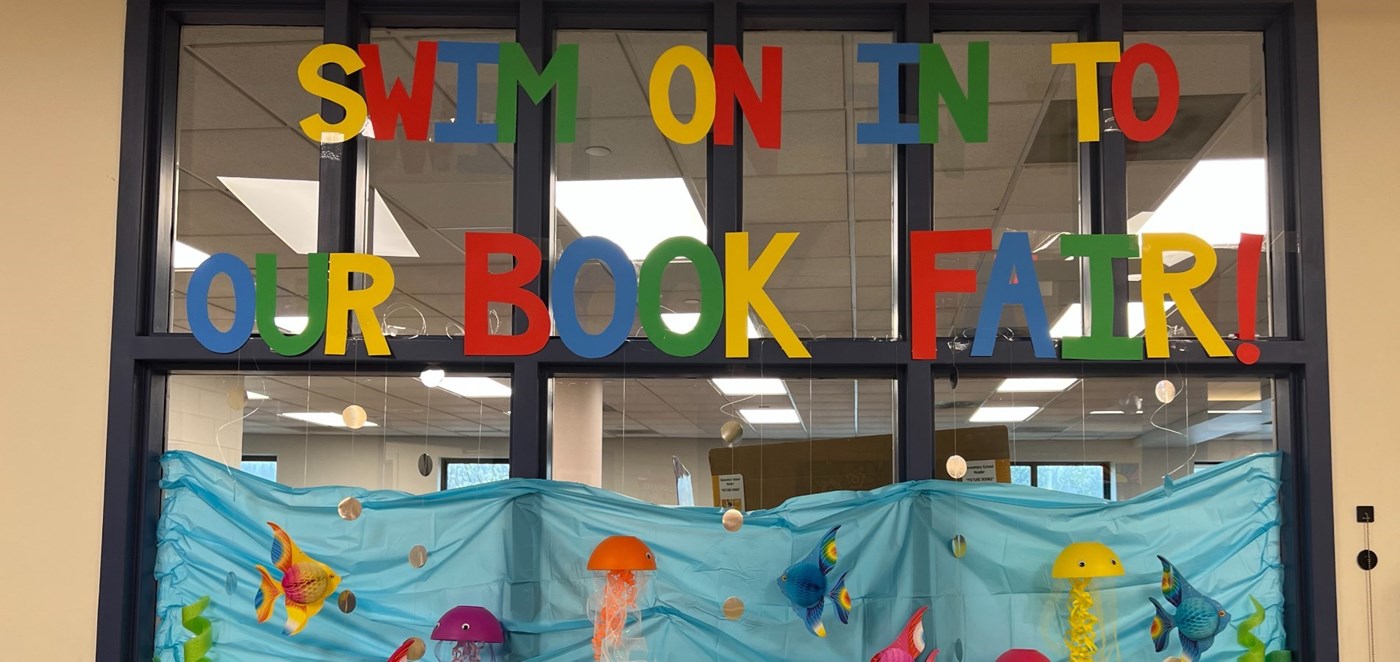A sign for the PTO Spring Book Fair that says &#34;Swim on In to Our Book Fair