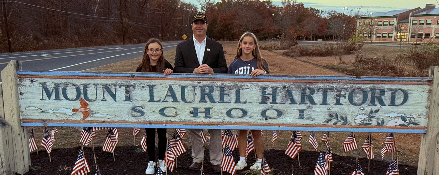 Retired Colonel Dennis Devery with Student Council Members standing behind Hartford sign with American flags